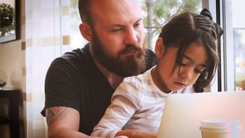 A young caucasian man in his 20s spending quality bonding time with a little 5 year old hispanic girl with long black hair and brown eyes as he teaches her how to use a laptop computer in a well lit cheerful room