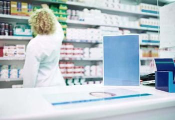 Shot of a blank board on the counter of a pharmacy with a pharmacist working in the background