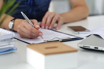 Close-up of female hands. Woman writting something and looking at mobile phone screen sitting at her office