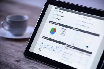 Charts and analytical data on the tablet screen with a cup of coffee on a wooden vintage table.