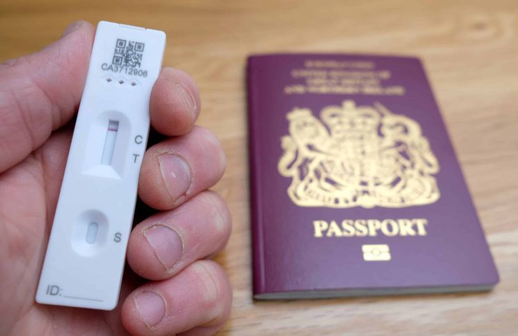 File photo dated 07/05/21 of a person holding a negative lateral flow Covid-19 test in front of a passport for the United Kingdom of Great Britain and Northern Ireland. New rules will come into force from October 24, in time for families returning from half-term breaks, allowing travellers arriving in England to take cheaper lateral flow tests rather than PCR test. Travellers who take a test at home must take a photo of their test and booking reference, and send this to the private test provider to verify the results. Transport Secretary Grant Shapps has said the change in policy for the post-arrival test is "based on trust". Issue date: Friday October 15, 2021.