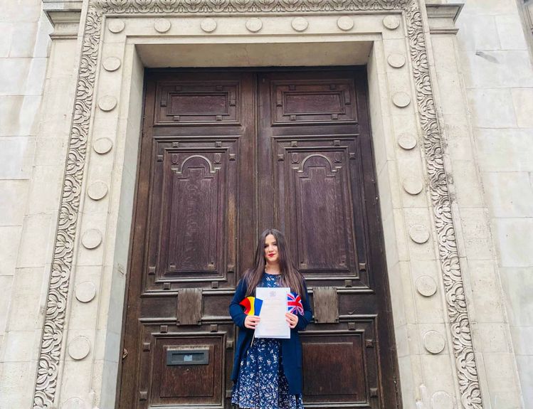 Journalist Andra Maciuca holding her British citizenship certificate and the flags of Romania and the UK.