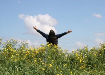 A man with long hair standing in a field of dasies.