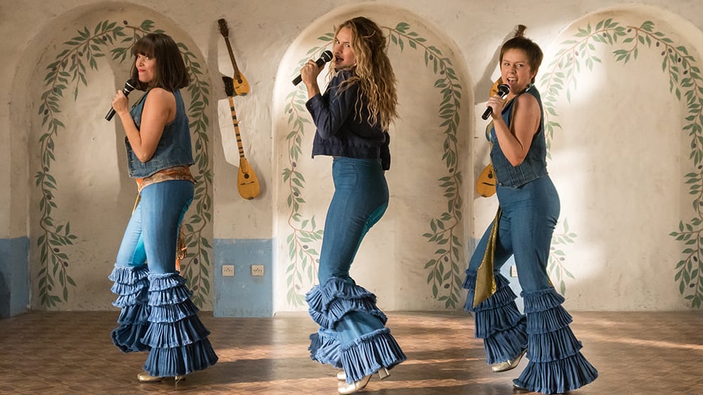 (L to R) Young Tanya (JESSICA KEENAN WYNN), Young Donna (LILY JAMES) and Young Rosie (ALEXA DAVIES) in "Mamma Mia! Here We Go Again."  Ten years after "Mamma Mia! The Movie," you are invited to return to the magical Greek island of Kalokairi in an all-new original musical based on the songs of ABBA.