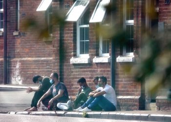 A group of men, thought to be migrants, sit outside in the sunshine after arriving yesterday night at Napier Barracks in Folkestone, Kent. Migrants will be housed in the military barracks from this week while their asylum claims are processed.