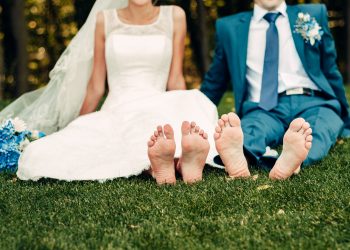 barefooted young fair-haired bride and her fiance sits on the grass in an exotic park, in a long white dress with a bouquet of flowers in her hands, a walk after the wedding ceremony, a wedding ceremony